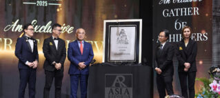 Group of formally dressed men and women on a stage, standing beside a framed award plaque labeled Asia Records, with a large event backdrop reading RECORDS and An Exclusive Gatherer text