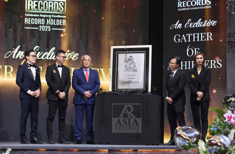 Group of formally dressed men and women on a stage, standing beside a framed award plaque labeled Asia Records, with a large event backdrop reading RECORDS and An Exclusive Gatherer text