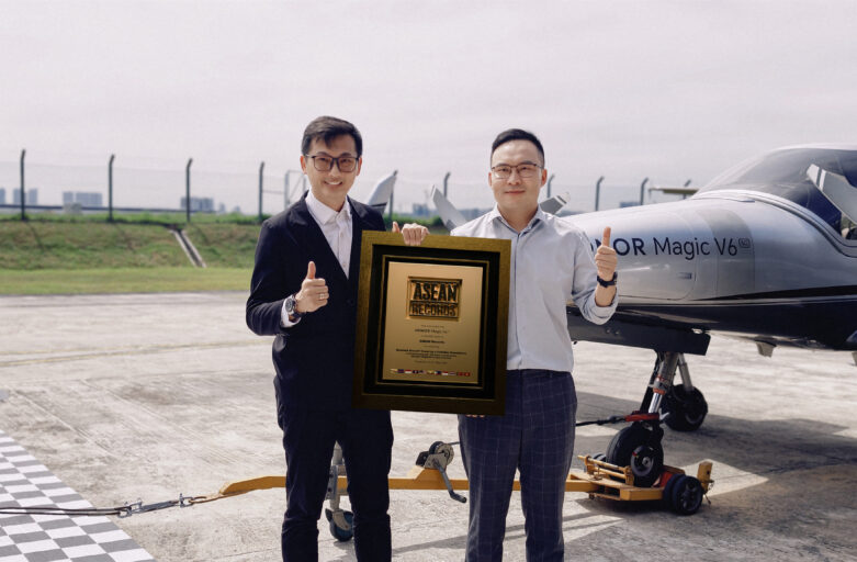 Two men in suits pose with an ASEAN Records plaque beside a small aircraft on a runway, thumbs up.