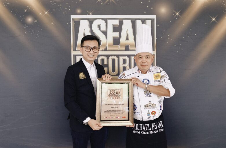Two men pose with a framed ASEAN Records certificate at an awards event, one in a suit, the other in a chef's uniform and hat.