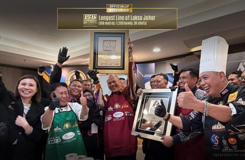 Celebration scene with chefs and staff holding a framed ASEAN Records certificate for the 'Longest Line of Laksa Johor' and giving thumbs up.