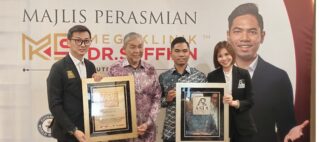 Four people in business attire pose with framed awards at an event, standing in front of a banner with a large portrait on the right.