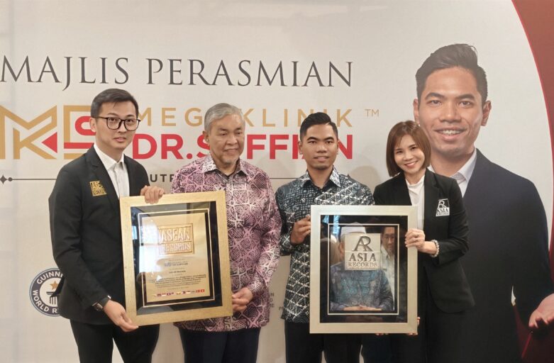 Four people in business attire pose with framed awards at an event, standing in front of a banner with a large portrait on the right.