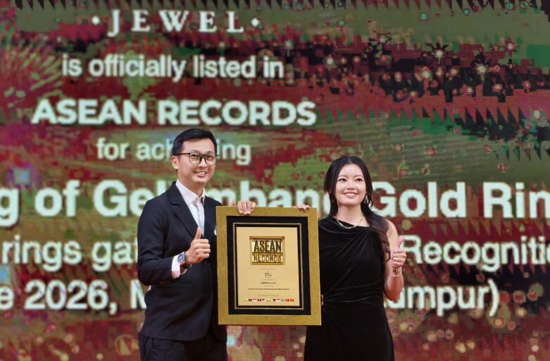 Two presenters pose with a framed ASEAN Records award on stage, smiling at the ceremony with a large, text-filled screen behind them.