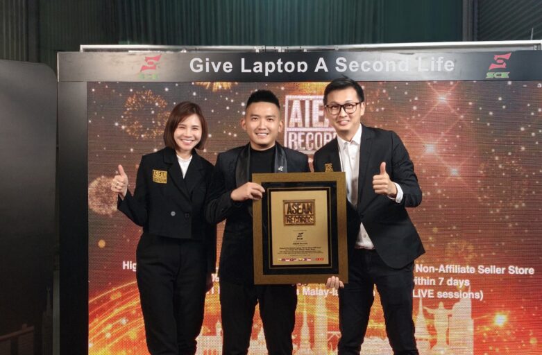 Three people in black attire posing with a framed award on a lit stage backdrop that reads 'Give Laptop A Second Life.'