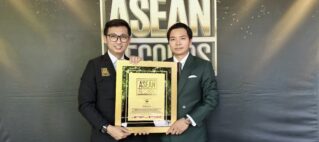 Two men in formal suits pose together holding a gold-framed award plaque that reads ASEAN Records, with a large ASEAN-themed backdrop behind them.