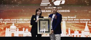 Two presenters pose on a stage holding a framed ASEAN Records award, smiling with a festive backdrop behind them.
