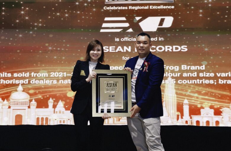 Two presenters pose on a stage holding a framed ASEAN Records award, smiling with a festive backdrop behind them.