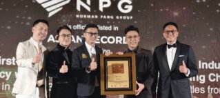Five men in formal attire pose on stage with a large framed award plaque, giving thumbs up at an award ceremony.