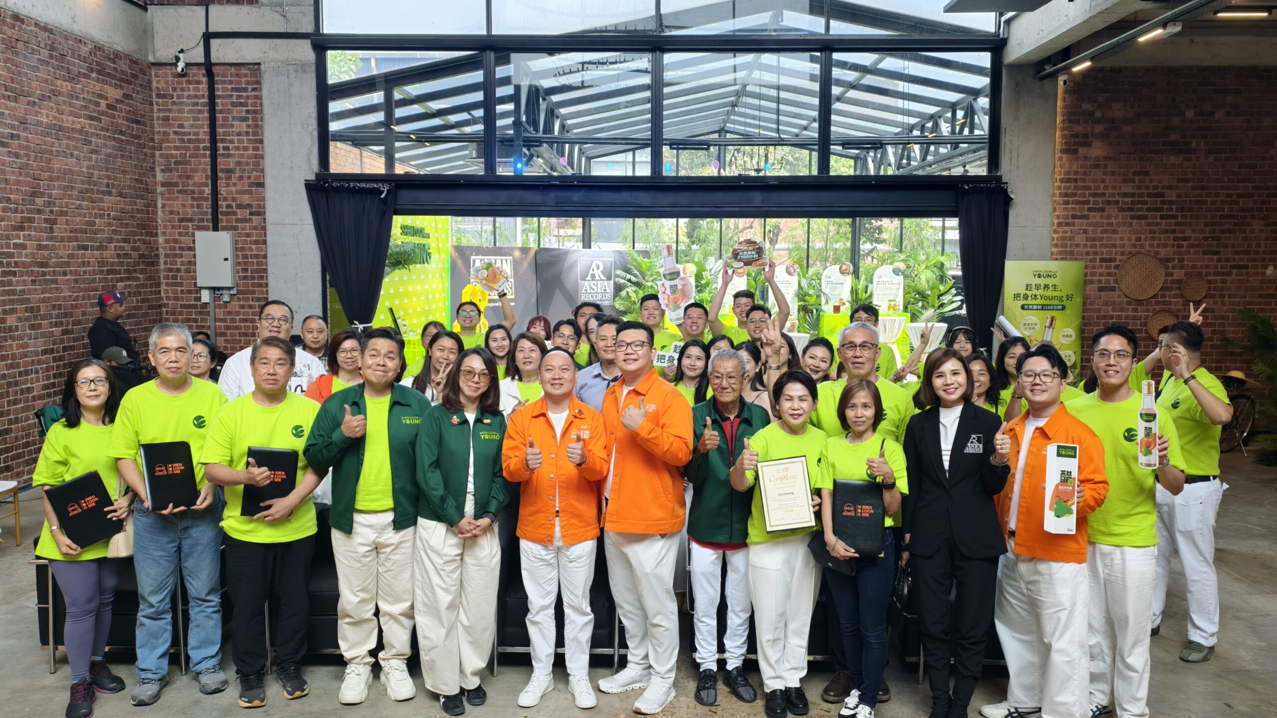 Large group of people in lime shirts posing for a group photo at an indoor event with brick walls and glass ceiling.