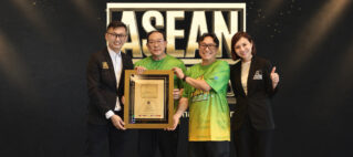 Four people in business attire pose with a framed award in front of a dark backdrop with large ASEAN lettering behind them.