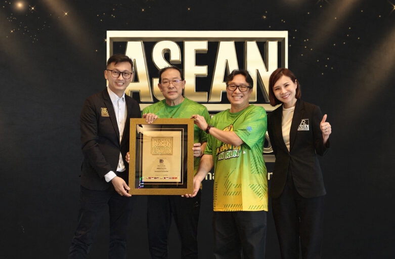 Four people in business attire pose with a framed award in front of a dark backdrop with large ASEAN lettering behind them.