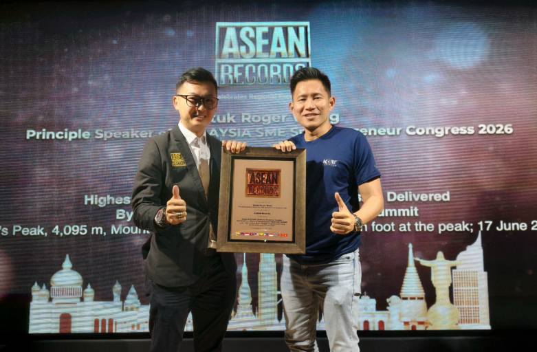 Two men on stage holding a framed award plaque with an ASEAN Records backdrop behind them. One wears a suit, the other a blue shirt, both giving a thumbs up to celebrate the award.