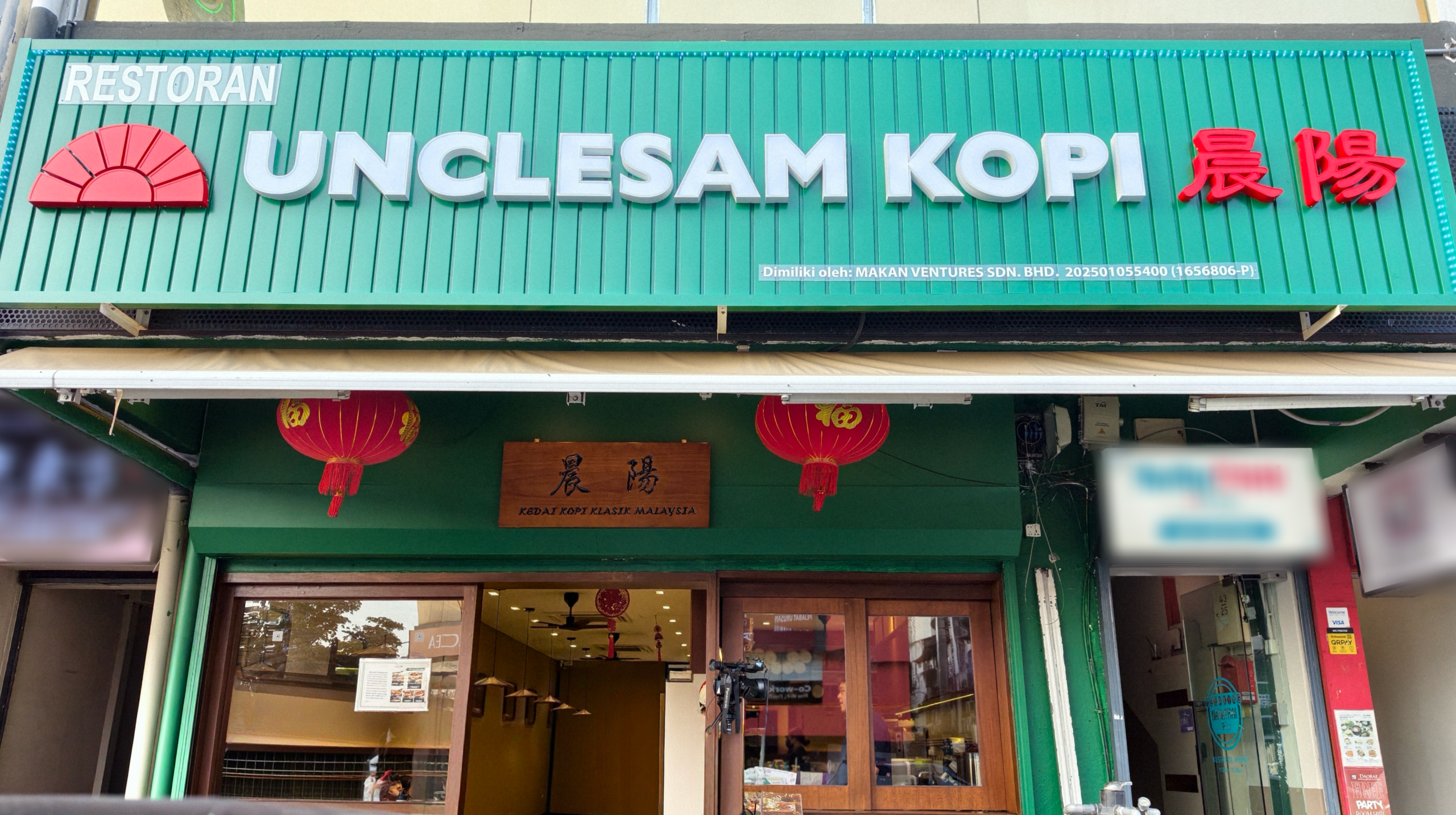 Storefront sign for 'UNCLESAM KOPI' restaurant and coffee shop on a green facade with red Chinese characters and a sun logo.