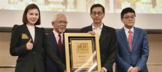 Four people in formal attire pose on stage, holding a large framed award plaque reading ASEAN Records in front of a cityscape backdrop.