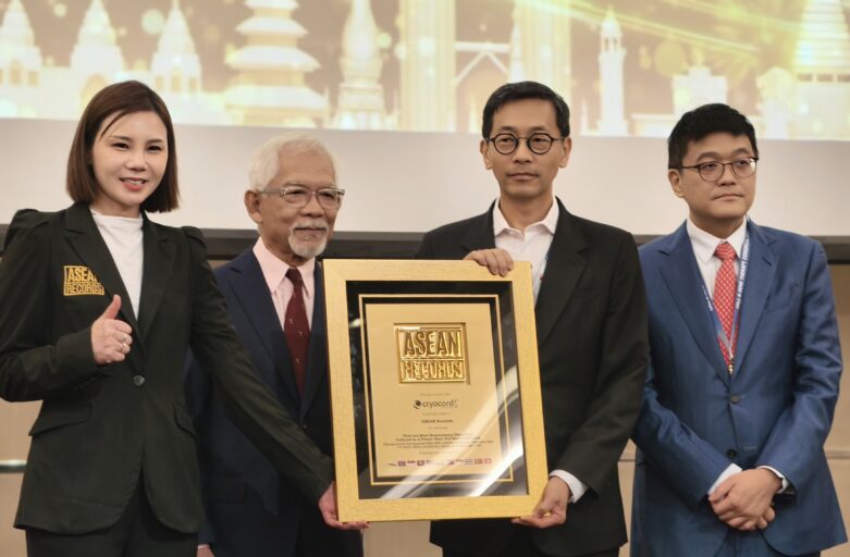 Four people in formal attire pose on stage, holding a large framed award plaque reading ASEAN Records in front of a cityscape backdrop.