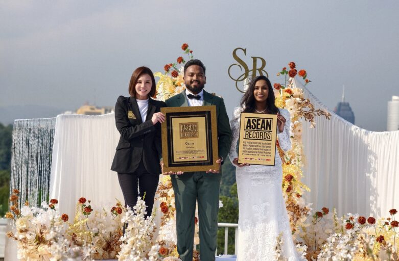 Three award recipients pose on a flower-decorated stage holding plaques, with a city skyline in the background.