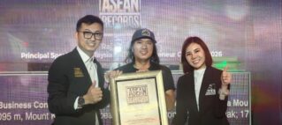 Three people on stage pose with a large framed ASEAN Records certificate, smiling in front of a colorful backdrop.